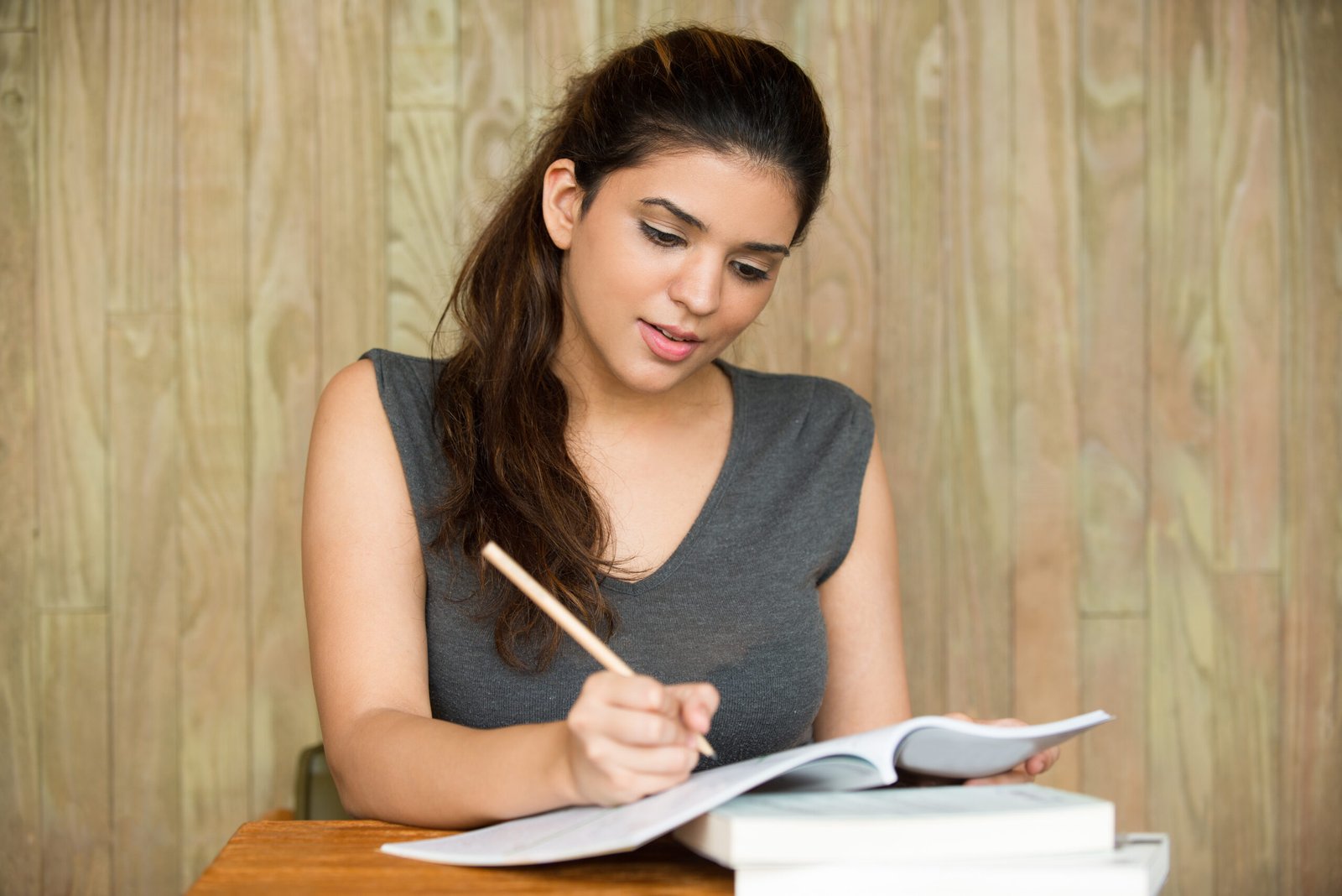 Portrait of young Caucasian female student sitting at desk, writing in copybook and smiling in classroom